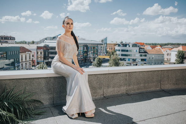 An adult woman wearing an elegant dress and sitting on a roof wall in Bosnia and Herzegovina - 写真・画像