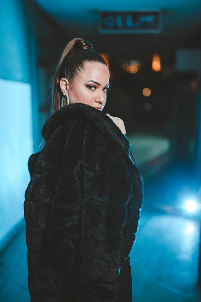 A vertical shot of a Caucasian female posing in a black fur at night - Photo, Image