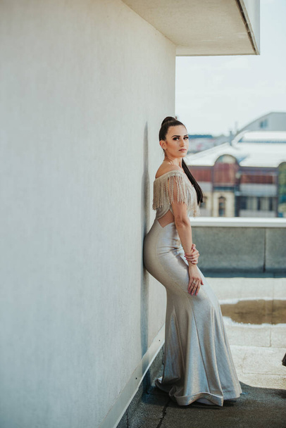 A vertical shot of a brunette female posing on a roof in a gorgeous beige evening dress - Foto, afbeelding