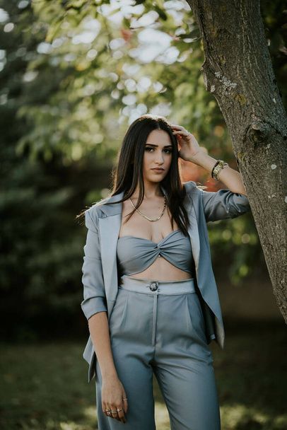 A young sexy Caucasian girl in a grey suit leaning on a tree in the garden - Foto, afbeelding