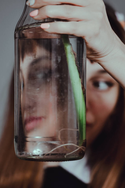 A vertical shot of a caucasian female holding a glass bottle with a green plant against her face - Fotó, kép