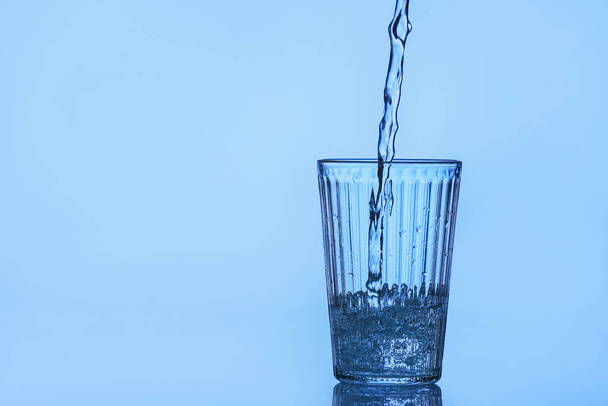Pouring of water into glass on color background - Foto, Bild
