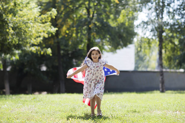 child girl with an American flag on outdoor. Independence Day. The United States celebrates July 4. - Фото, зображення