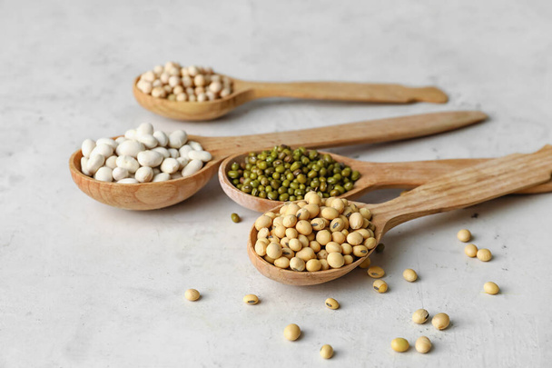 Spoons with different legumes on light background, closeup - Photo, image