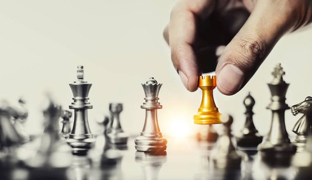 Obchodní strategie, strategické plánování. Lidská ruka drží zlatou šachovou figurku hraje hru na šachmat soupeře na šachovnici. - Fotografie, Obrázek