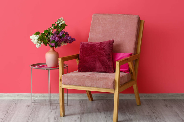 Stilvoller Sessel und Vase mit fliederfarbenen Blumen in der Nähe der Wand - Foto, Bild