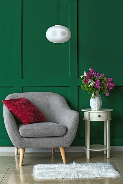 Крісло і ваза з бузковими квітами біля кольорової стіни. - Фото, зображення