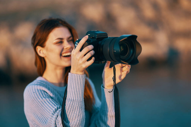 woman holding a camera with a lens in nature in the mountains and the sea  - Foto, imagen