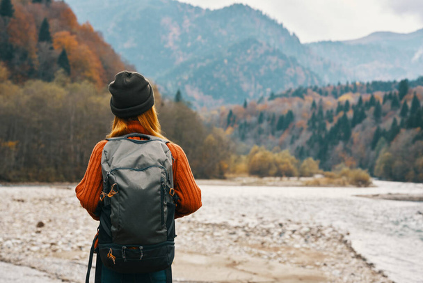mujer viaja en las montañas en otoño cerca del río en la naturaleza con una mochila vista trasera - Foto, imagen