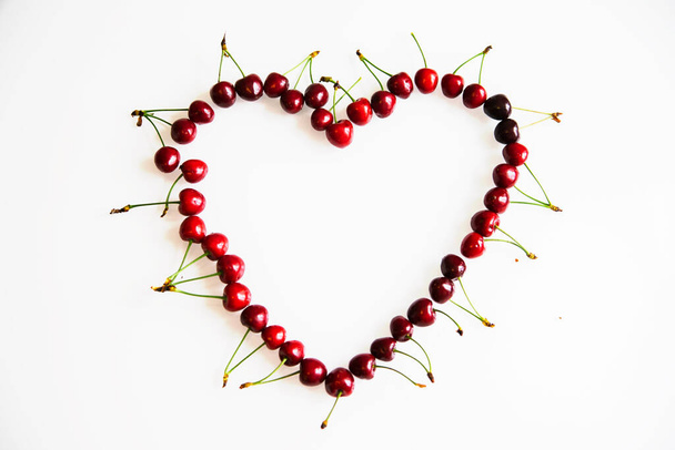 Red ripe cherries laid out in the shape of a heart on a white background. Summer background of juicy fruits.Valentine's Day. The concept of romance and love. - Foto, immagini