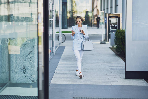 Adult attractive woman with smartphone walking in the city - Photo, Image
