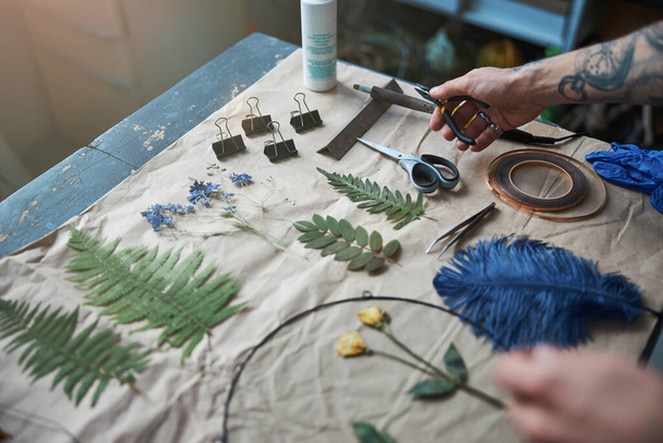 Joven sosteniendo alicates y haciendo herbario en taller - Foto, imagen