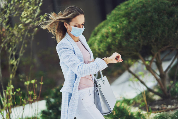 Mujer atractiva adulta en máscara con teléfono inteligente caminando en la ciudad - Foto, imagen
