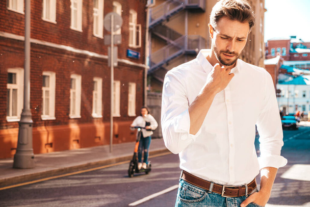 Portrait of handsome confident stylish hipster lambersexual model.Modern man dressed in white shirt. Fashion male posing on the street background. Outdoors at sunset  - Foto, Imagem