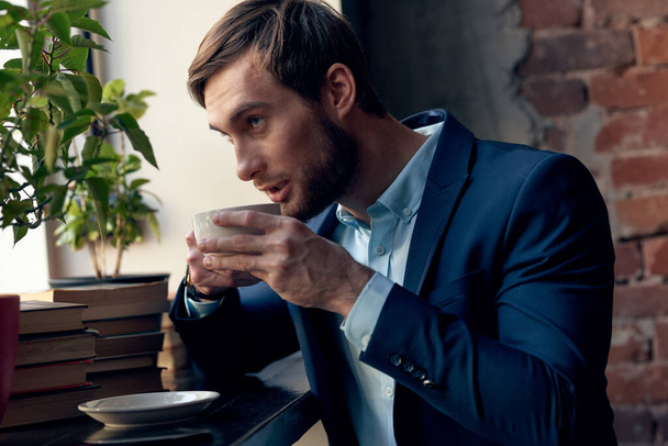 ein Mann im Anzug trinkt Kaffee am Fenster eines Cafés. - Foto, Bild