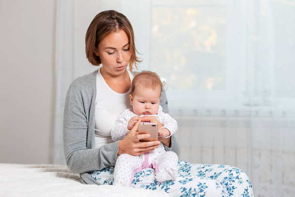 A mother holds a child in her arms and shows him something on her smartphone. Copy space. The concept of teaching and entertaining children using a smartphone. - Φωτογραφία, εικόνα