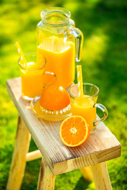 Due bicchieri di gustoso succo d'arancia appena spremuto sullo sgabello da giardino sul prato verde - Foto, immagini