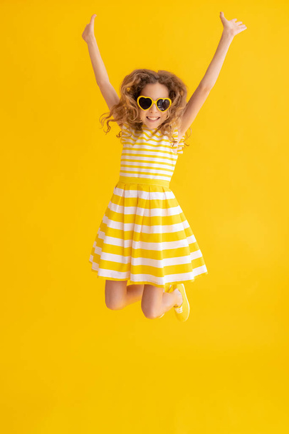 Happy child jumping against yellow summer background. Portrait of cheerful girl. Success and winner concept - Photo, image