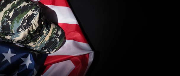 Militärhut oder -tasche mit amerikanischer Flagge. Soldatenmütze oder -helm mit amerikanischer Nationalflagge auf schwarzem Hintergrund. Militärisches Konzept durch Tarnobjekt und USA-Nationalflagge vertreten. - Foto, Bild