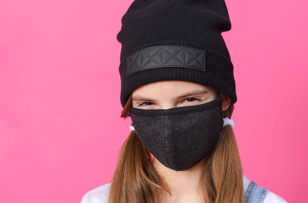 white teenage girl in black mask and hat on pink background - Фото, зображення