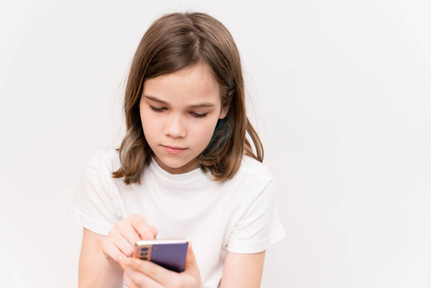 The teenage girl types text in a smartphone on a white background. children's dependence on gadgets and social networks. - Foto, imagen