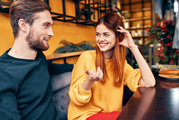handsome man and happy woman in sweater are sitting at a table in a cafe chatting room interior - Photo, Image