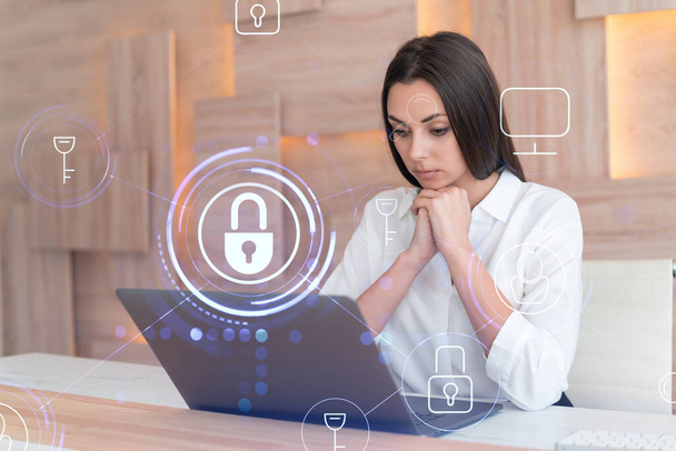 Attractive businesswoman in white shirt at workplace working with laptop to defend customer cyber security. Concept of clients information protection. Padlock hologram over office background. - Φωτογραφία, εικόνα