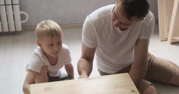 Тато і маленький син малюють стіл, тумбочку. Дитина допомагає батькові. Денне світло
. - Кадри, відео