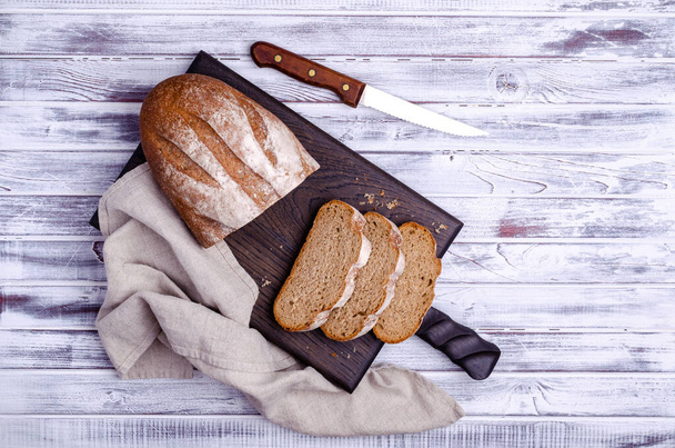 Традиционный темный хлеб на светлом деревянном фоне. Вид сверху. - Фото, изображение