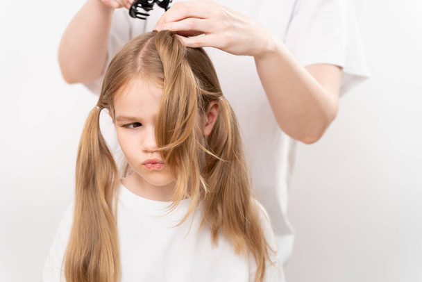 woman combs and does the hair of a clittle girl on a white background. Mommy is a hairdresser. saving money at a beauty salon. shampoos and cosmetics for children's hair. - Valokuva, kuva