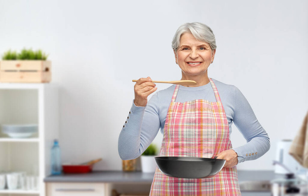 smiling senior woman with frying pan at kitchen - Zdjęcie, obraz
