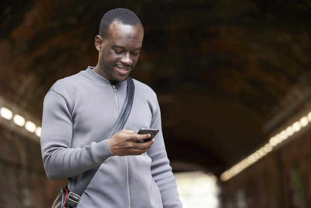 Smiling Young Man In Urban Setting Checks Messages And Social Media On Mobile Phone  - 写真・画像