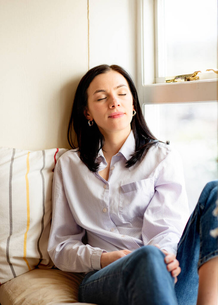 woman in white shirt dreaming on windowsill in home - Фото, изображение