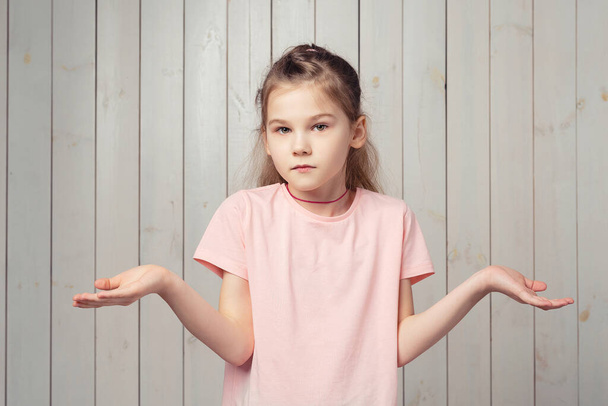 I donT know. Indecisive little girl 9-11 years old shrugging shoulders, looking innocent, cant tell anything, have no idea nothing to say, standing puzzled against wooden background - Foto, Imagem