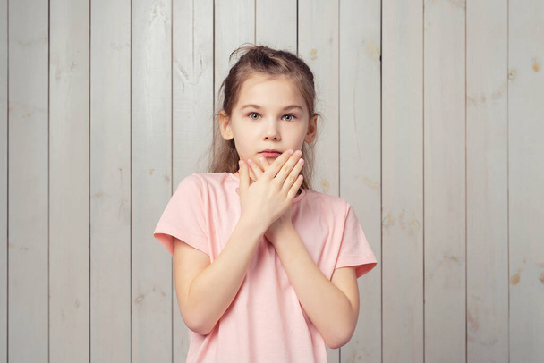 Eu tenho medo. Menina assustada 9-11 anos de idade em camisa casual rosa t, é tampa abriu palmas da boca e olhando assustado e ansioso para a câmera, temer algo, de pé contra o fundo de madeira - Foto, Imagem