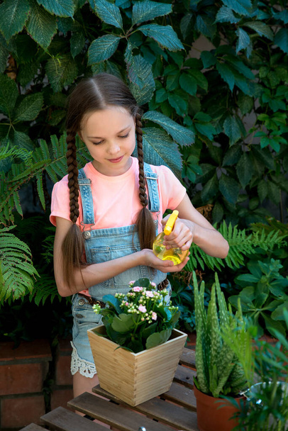 Little cute girl watering flowers in the family garden at a summer day. Kid sprays indoor flowers. - Valokuva, kuva