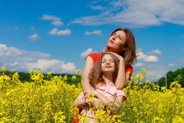 Moeder en dochter in de natuur buiten levensstijl. Vrolijke bliksem gele kleur van bloeiende koolzaad veld op de achtergrond. Geluk plezier concept. - Foto, afbeelding