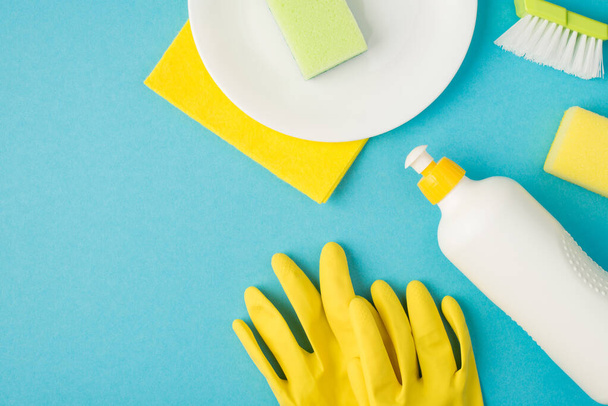 Overhead-Foto von Teller Schwamm Pinsel Seife Reinigungstuch und gelbe Handschuhe isoliert auf dem blauen Hintergrund - Foto, Bild
