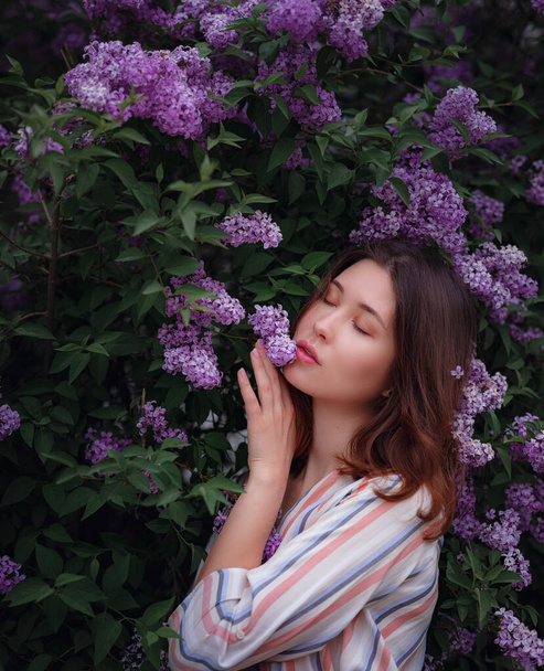 beautiful young asian woman enjoying the blooming of flowers lilac in spring. Nude make up. Close up portrait in beautiful purple lilac bushes - 写真・画像