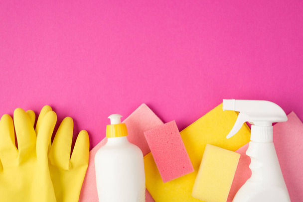 Góra widok zdjęcie różowy i żółty wiskoza szmaty gumowe rękawice gąbki biały spray i żel butelki detergentu na odizolowanym różowym tle z pustym miejscu - Zdjęcie, obraz