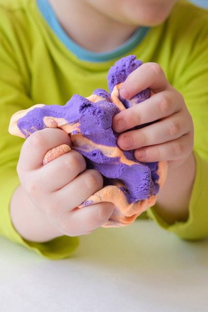 detailní záběr dětských ručiček mačkajících měkký plasticin. Koncept je rozvoj kreativního myšlení a jemných motorických dovedností, udržování tónu rukou, úleva od stresu. svislá fotografie. - Fotografie, Obrázek