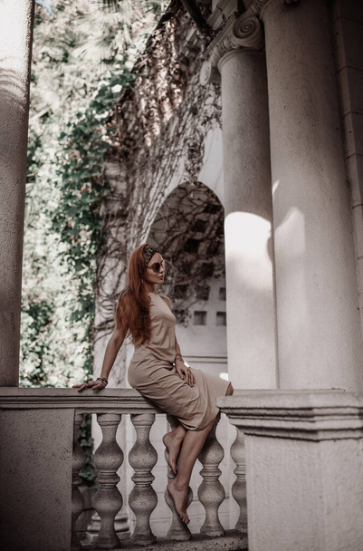 Young woman tourist in summer dress is sitting on ancient balustrade of old palace terrace looking at classic column - Foto, Bild
