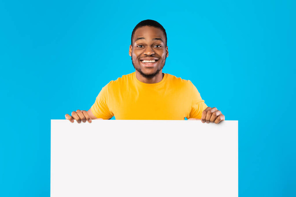 Czarny facet trzyma pustą tablicę białą księgę na niebieskim tle - Zdjęcie, obraz