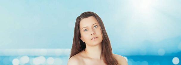 Cuidado de la piel y protección solar en verano. Retrato de una hermosa joven bronceada, azul mar y cielo sobre fondo, belleza, bienestar y concepto de viaje - Foto, Imagen