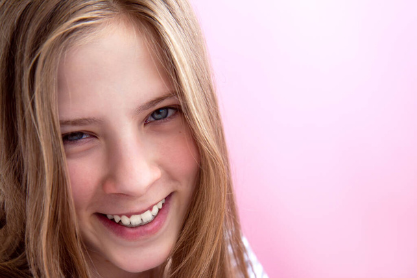Обличчя красивої усміхненої дівчини-підлітка з довгим волоссям на рожевому фоні
 - Фото, зображення