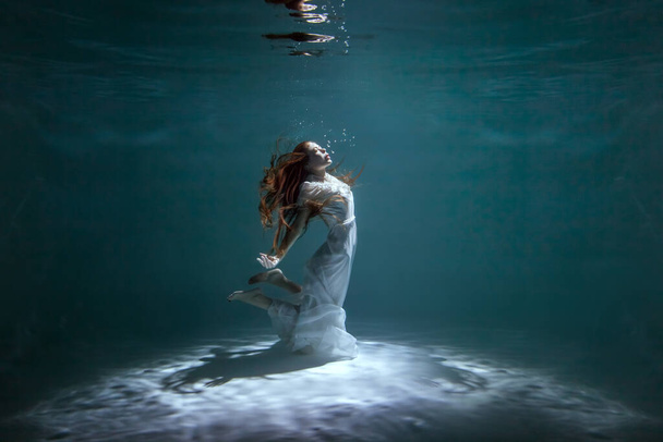 Mulher de vestido branco está dançando debaixo d 'água enquanto mostra um show. - Foto, Imagem
