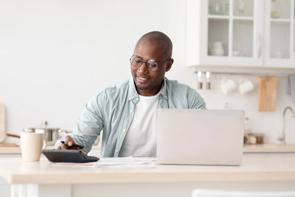 Pagando contas, impostos em casa on-line durante a pandemia do covid-19. Homem americano africano maduro com documentos e laptop - Foto, Imagem