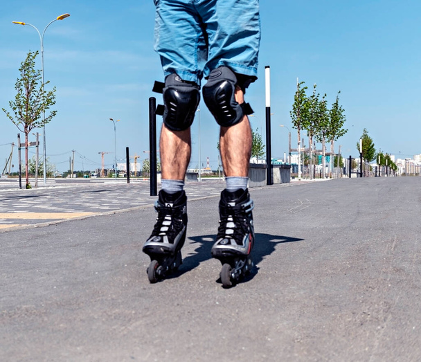 Patas masculinas en patines y equipo de protección de cerca montar en la carretera de asfalto en verano, patinaje sobre ruedas - Foto, imagen