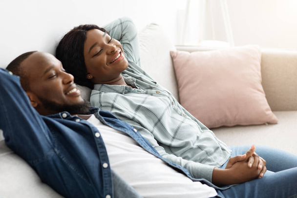 Hora de relajarse. Feliz pareja negra descansando en cómodo sofá en casa - Foto, Imagen