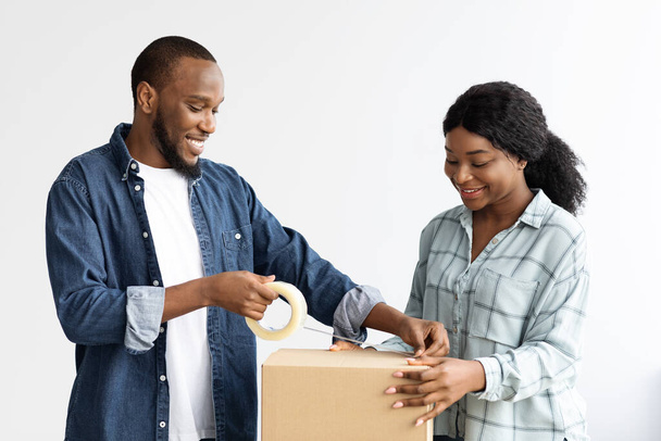 feliz pareja negra embalaje pertenencias en caja antes de mudarse a nuevo hogar - Foto, imagen